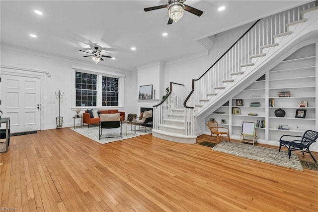 living room with crown molding, built in features, ceiling fan, and hardwood / wood-style flooring