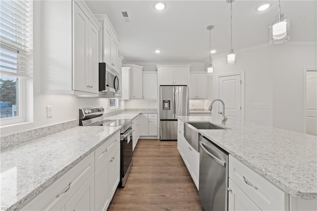 kitchen with hanging light fixtures, a center island with sink, stainless steel appliances, light stone countertops, and white cabinets