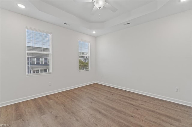 unfurnished room with a raised ceiling, hardwood / wood-style flooring, and ceiling fan