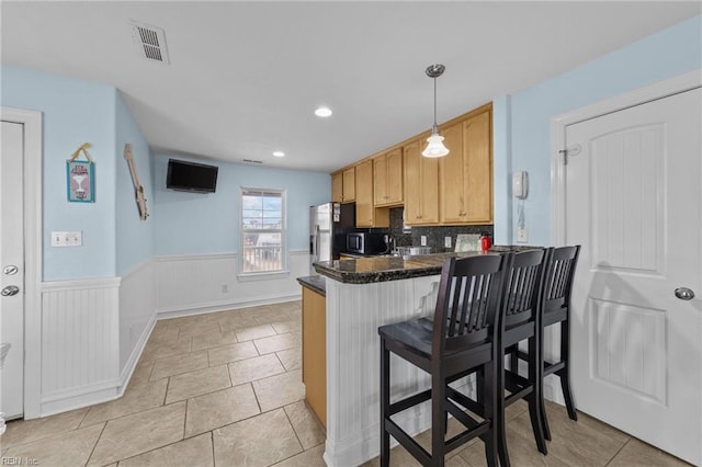 kitchen featuring appliances with stainless steel finishes, a breakfast bar, backsplash, hanging light fixtures, and kitchen peninsula