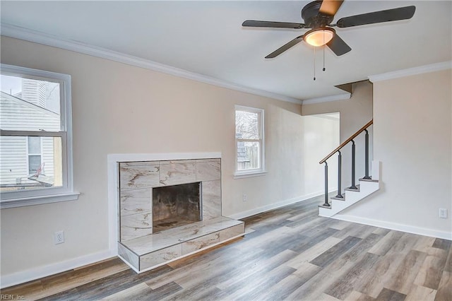 unfurnished living room featuring crown molding, wood-type flooring, ceiling fan, and a high end fireplace