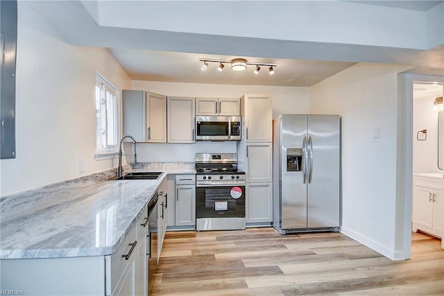 kitchen featuring appliances with stainless steel finishes, sink, gray cabinetry, light stone counters, and light wood-type flooring