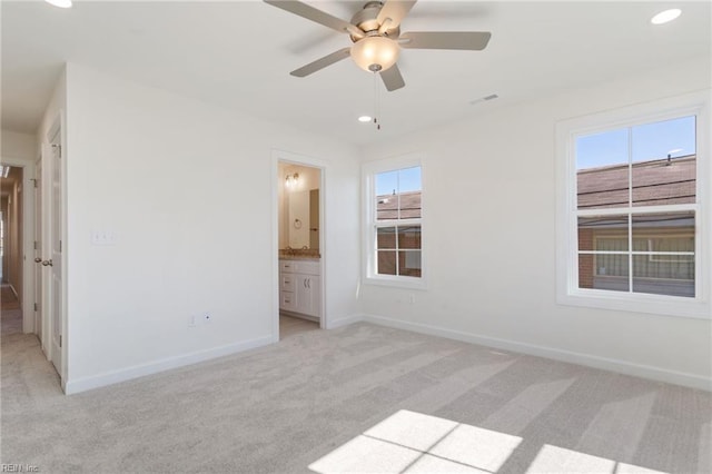 unfurnished bedroom with multiple windows, connected bathroom, light colored carpet, and ceiling fan