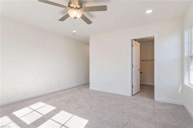 unfurnished bedroom featuring a walk in closet, light colored carpet, and ceiling fan