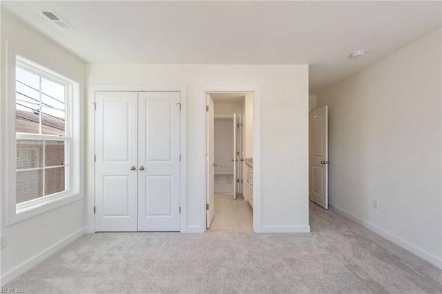 unfurnished bedroom featuring ensuite bathroom, light colored carpet, and a closet