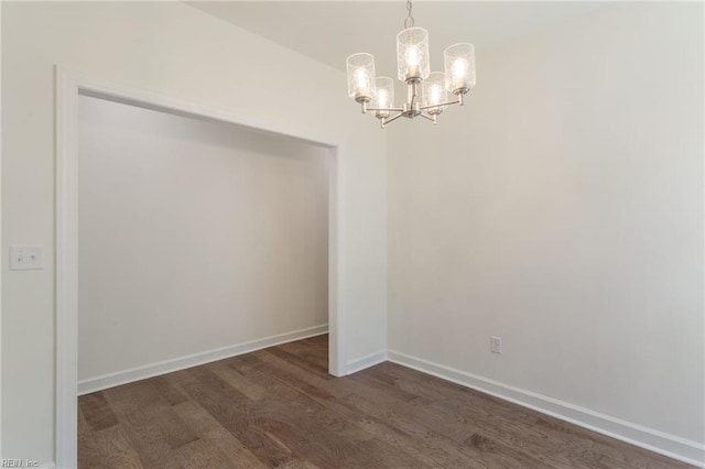 spare room with dark hardwood / wood-style flooring and an inviting chandelier