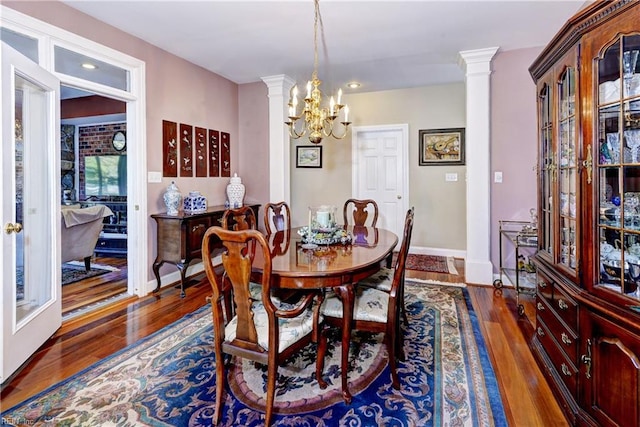 dining area with ornate columns, an inviting chandelier, and dark hardwood / wood-style flooring