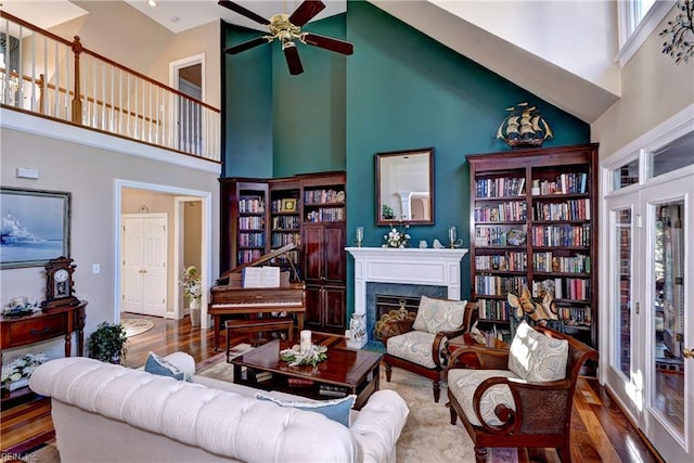 living room with hardwood / wood-style flooring, a towering ceiling, a high end fireplace, and ceiling fan