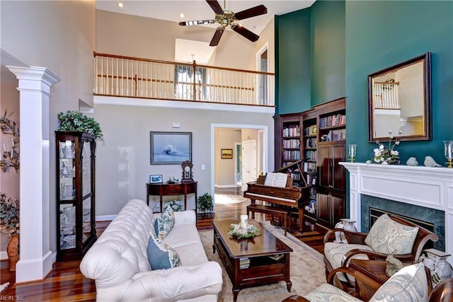 living room featuring ornate columns, wood-type flooring, ceiling fan, a premium fireplace, and a high ceiling