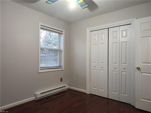 unfurnished bedroom featuring a baseboard heating unit, dark wood-type flooring, a closet, and ceiling fan