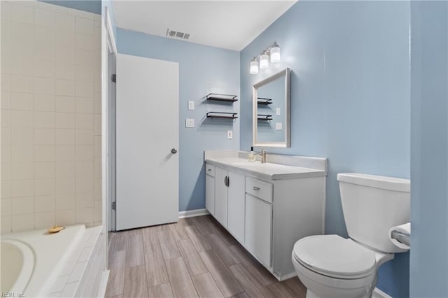 bathroom featuring vanity, a relaxing tiled tub, toilet, and hardwood / wood-style flooring