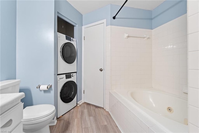 full bathroom featuring tiled shower / bath, stacked washer and clothes dryer, toilet, and wood-type flooring