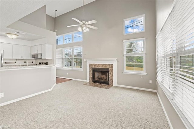 unfurnished living room featuring ceiling fan, light colored carpet, a healthy amount of sunlight, and a high ceiling