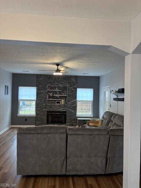 living room with ceiling fan, wood-type flooring, and a stone fireplace