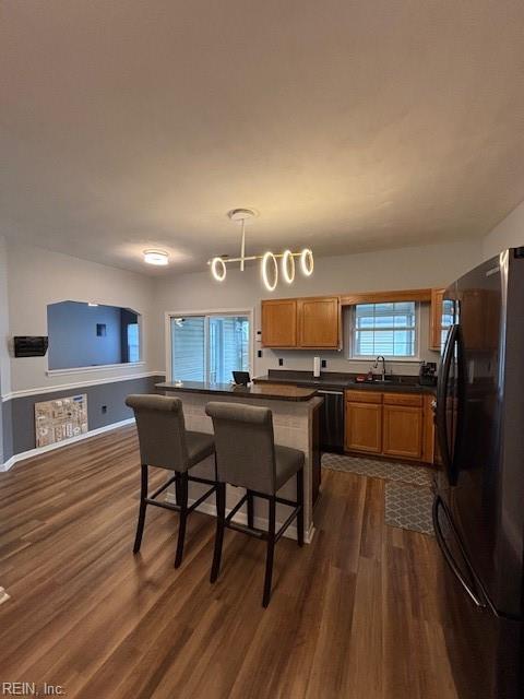 kitchen with dark hardwood / wood-style floors, pendant lighting, sink, a kitchen bar, and black appliances