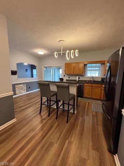 kitchen with pendant lighting, sink, a kitchen breakfast bar, black appliances, and dark hardwood / wood-style flooring