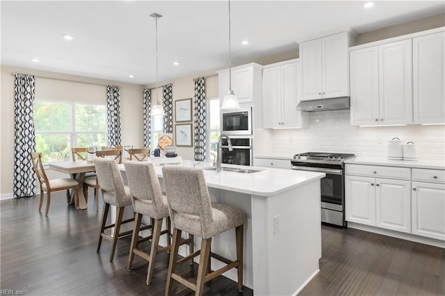 kitchen with white cabinetry, appliances with stainless steel finishes, decorative light fixtures, and a center island with sink