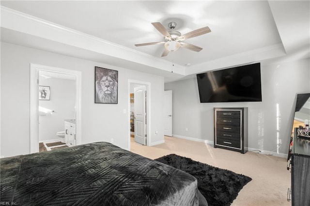 bedroom with ceiling fan, a tray ceiling, ensuite bath, and light carpet