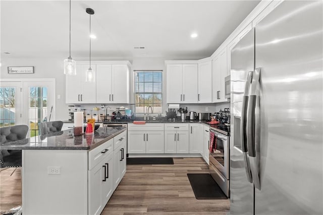 kitchen featuring dark stone countertops, appliances with stainless steel finishes, hanging light fixtures, and white cabinets