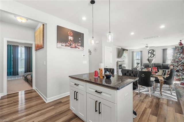 kitchen featuring hanging light fixtures, dark hardwood / wood-style floors, a center island, white cabinets, and dark stone counters