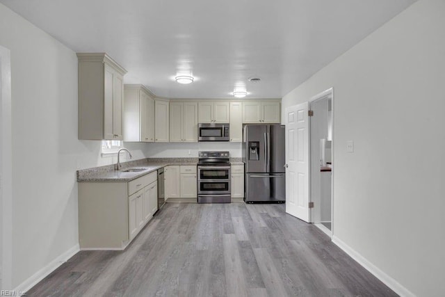 kitchen featuring stainless steel appliances, light stone countertops, sink, and light wood-type flooring