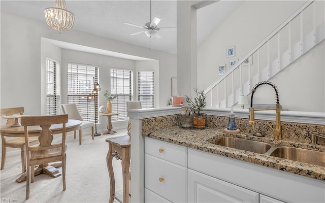 kitchen featuring sink, white cabinetry, decorative light fixtures, light carpet, and ceiling fan with notable chandelier