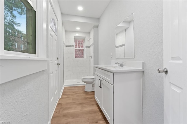 bathroom with a tile shower, vanity, hardwood / wood-style flooring, and toilet