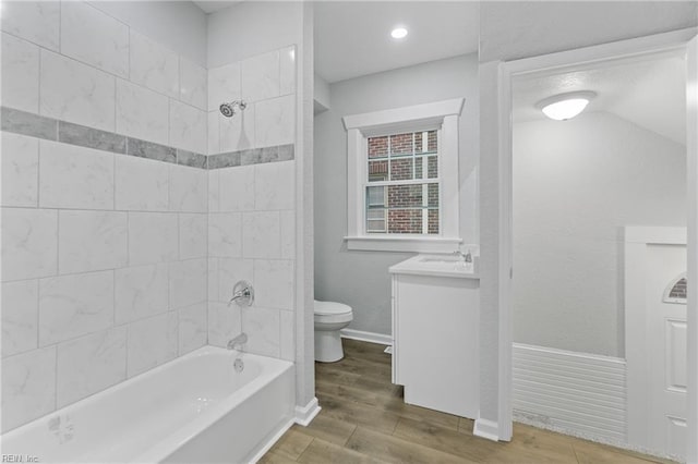 full bathroom with tiled shower / bath combo, vanity, hardwood / wood-style flooring, and toilet