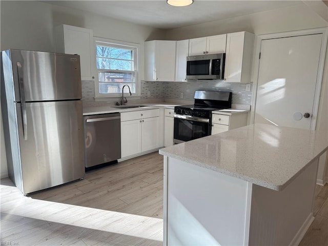 kitchen featuring appliances with stainless steel finishes, white cabinetry, sink, light stone countertops, and light wood-type flooring