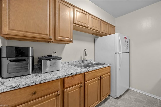 kitchen with white refrigerator, light stone countertops, and sink