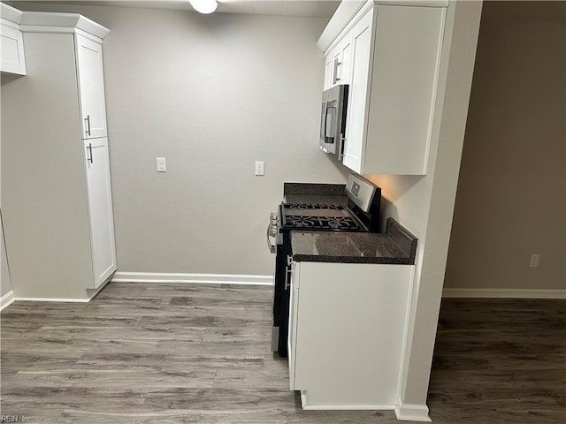 kitchen featuring hardwood / wood-style flooring, appliances with stainless steel finishes, dark stone countertops, and white cabinets