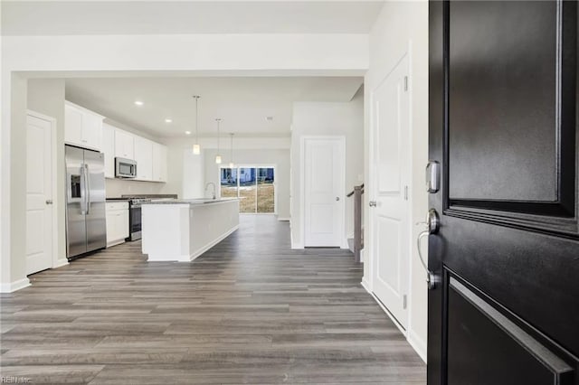 kitchen featuring decorative light fixtures, white cabinets, stainless steel appliances, dark wood-type flooring, and a center island with sink