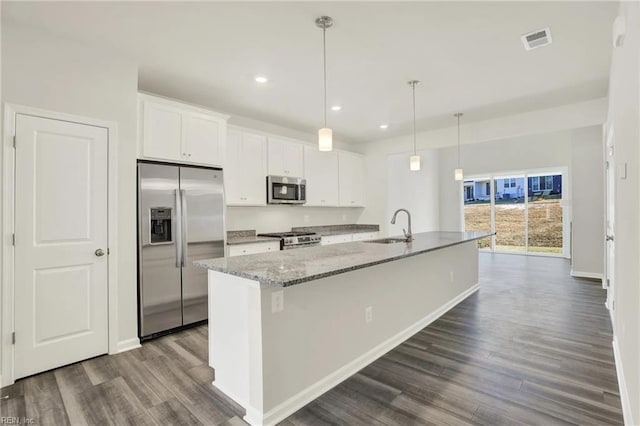 kitchen featuring white cabinets, hanging light fixtures, a kitchen island with sink, stainless steel appliances, and light stone countertops