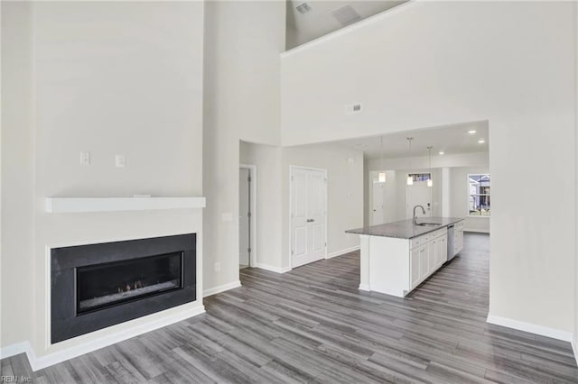 kitchen with sink, a kitchen island with sink, hanging light fixtures, dark hardwood / wood-style floors, and white cabinets