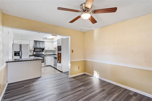 kitchen with kitchen peninsula, dark hardwood / wood-style floors, white cabinets, and appliances with stainless steel finishes