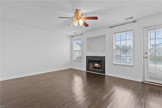 unfurnished living room featuring dark wood-type flooring, ceiling fan, and a wealth of natural light