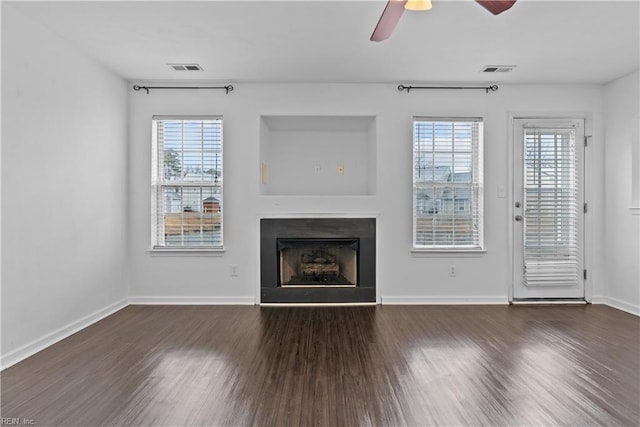 unfurnished living room featuring dark wood-type flooring, a wealth of natural light, and ceiling fan