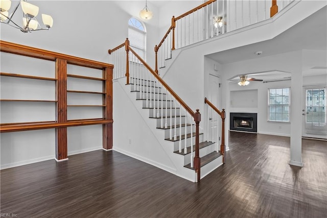 stairway with wood-type flooring, ceiling fan with notable chandelier, and a high ceiling