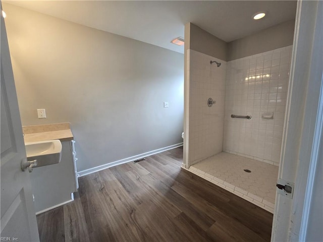 bathroom with wood-type flooring, a tile shower, vanity, and toilet