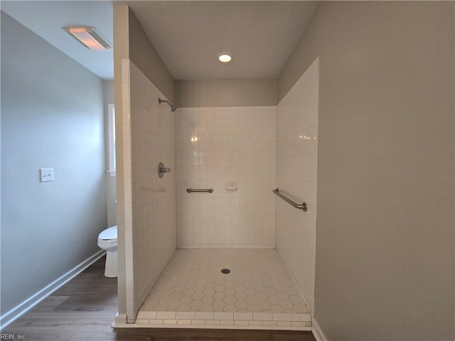 bathroom featuring hardwood / wood-style flooring, tiled shower, and toilet