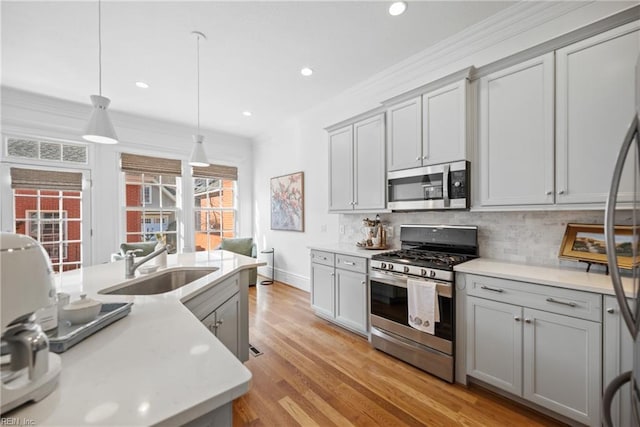 kitchen featuring tasteful backsplash, sink, gray cabinetry, hanging light fixtures, and stainless steel appliances