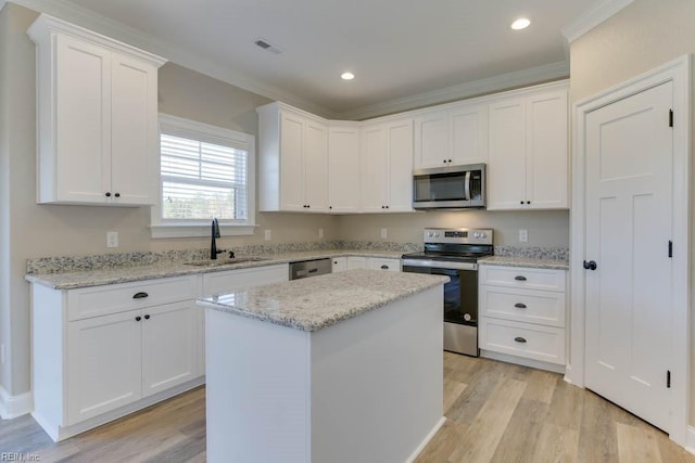 kitchen with sink, light stone counters, appliances with stainless steel finishes, a kitchen island, and white cabinets