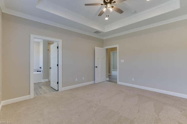 unfurnished bedroom featuring crown molding, connected bathroom, a tray ceiling, and light carpet