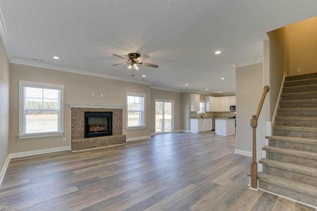 unfurnished living room with sink, light hardwood / wood-style flooring, ceiling fan, ornamental molding, and a brick fireplace