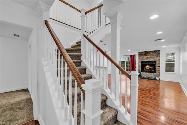 stairway featuring wood-type flooring, a stone fireplace, and ornamental molding