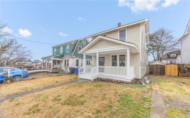 view of front of house featuring covered porch, a front lawn, a chimney, and fence