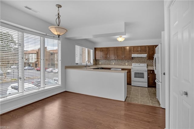 kitchen featuring pendant lighting, backsplash, hardwood / wood-style flooring, kitchen peninsula, and white appliances