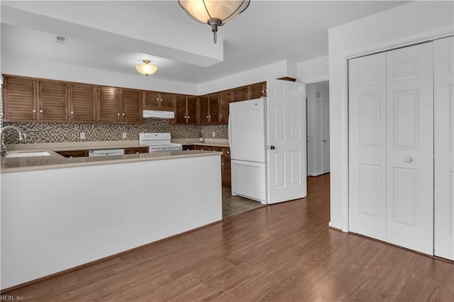 kitchen with dark hardwood / wood-style floors, sink, backsplash, kitchen peninsula, and white appliances