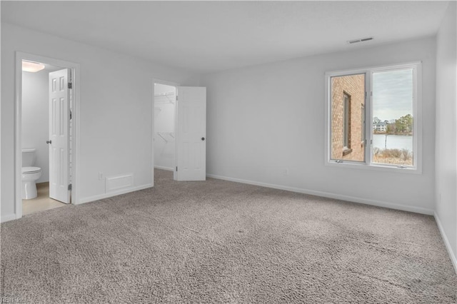 unfurnished bedroom featuring a spacious closet, ensuite bath, light colored carpet, and a closet