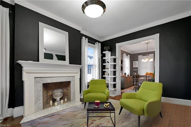 living area featuring a notable chandelier, wood-type flooring, ornamental molding, and a fireplace